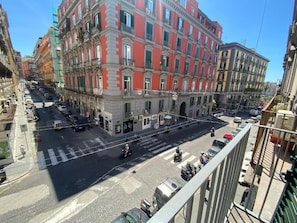 A street view with a building featuring a row of windows and balconies, a crosswalk, and parked cars. - LudBen Dante (Naples)