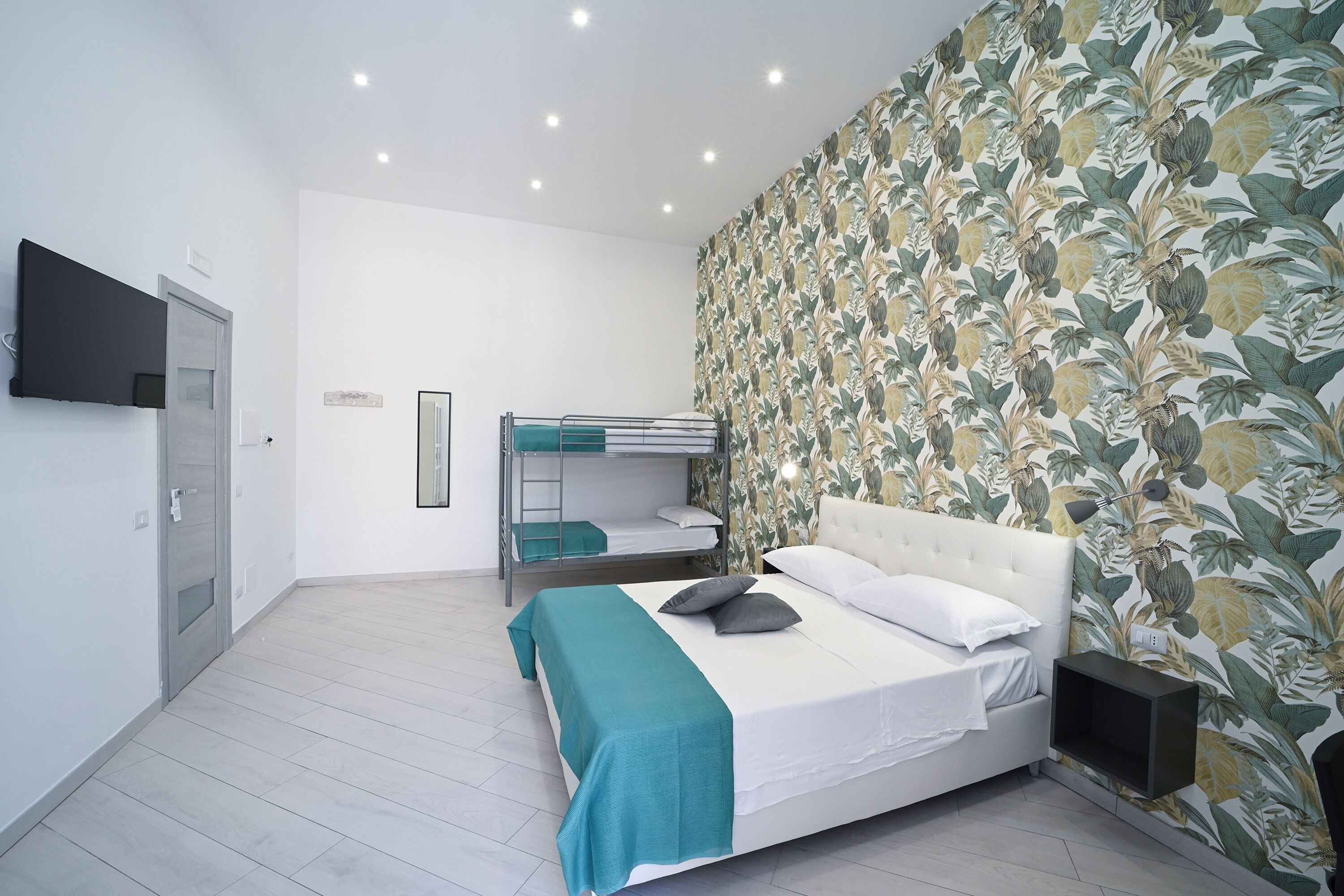 Une chambre avec un lit superposé, un lit simple, une télévision et un papier peint à motifs floraux.
