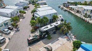 A waterfront property with multiple white buildings, a dock, and parked vehicles.