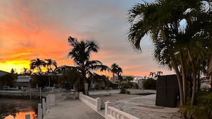 A waterfront area with a concrete walkway, palm trees, and a sunset.