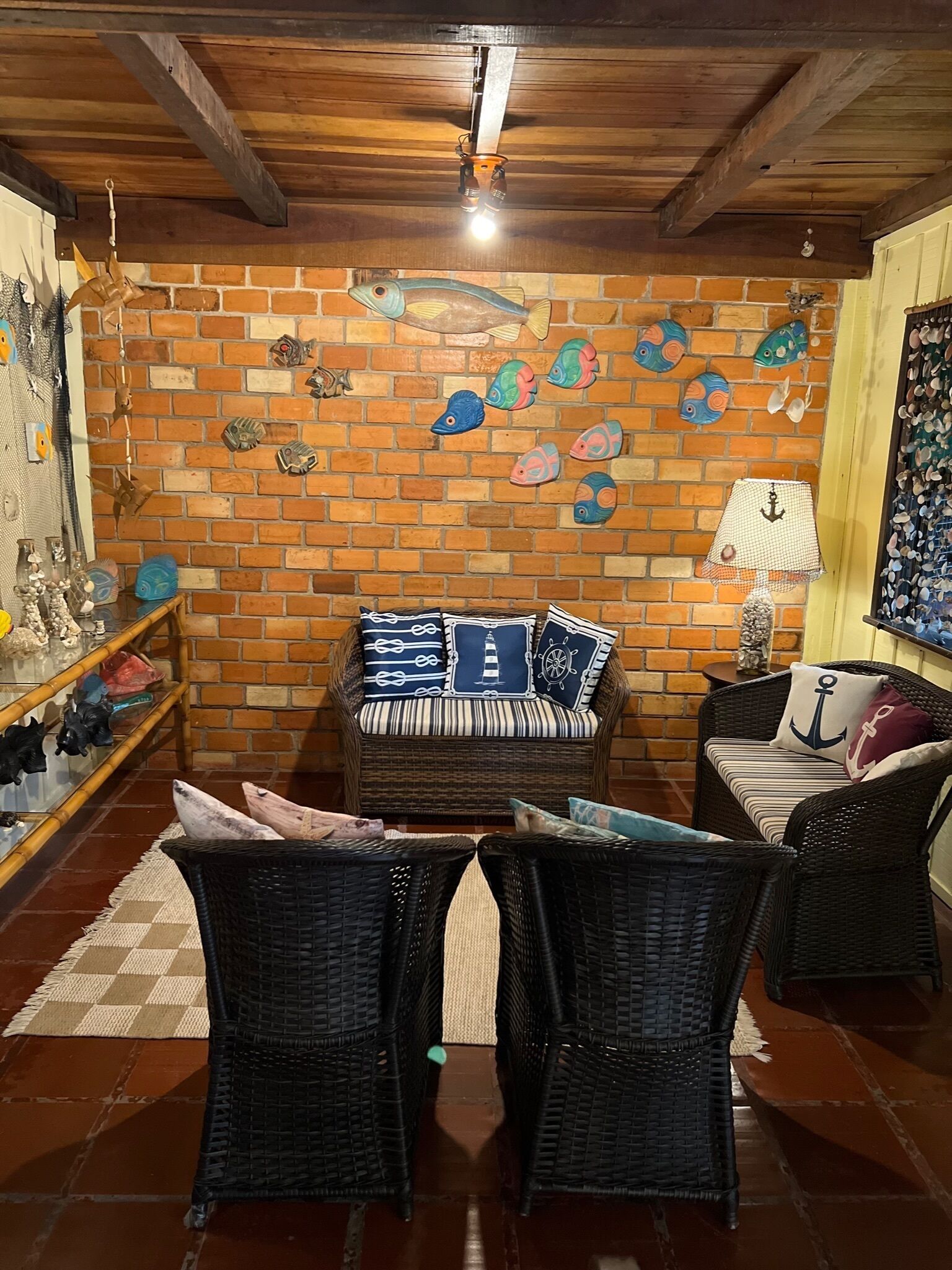 Une pièce chaleureuse avec un mur en briques orné de motifs de poissons et d’ancres, des meubles en osier et un plafond en bois.