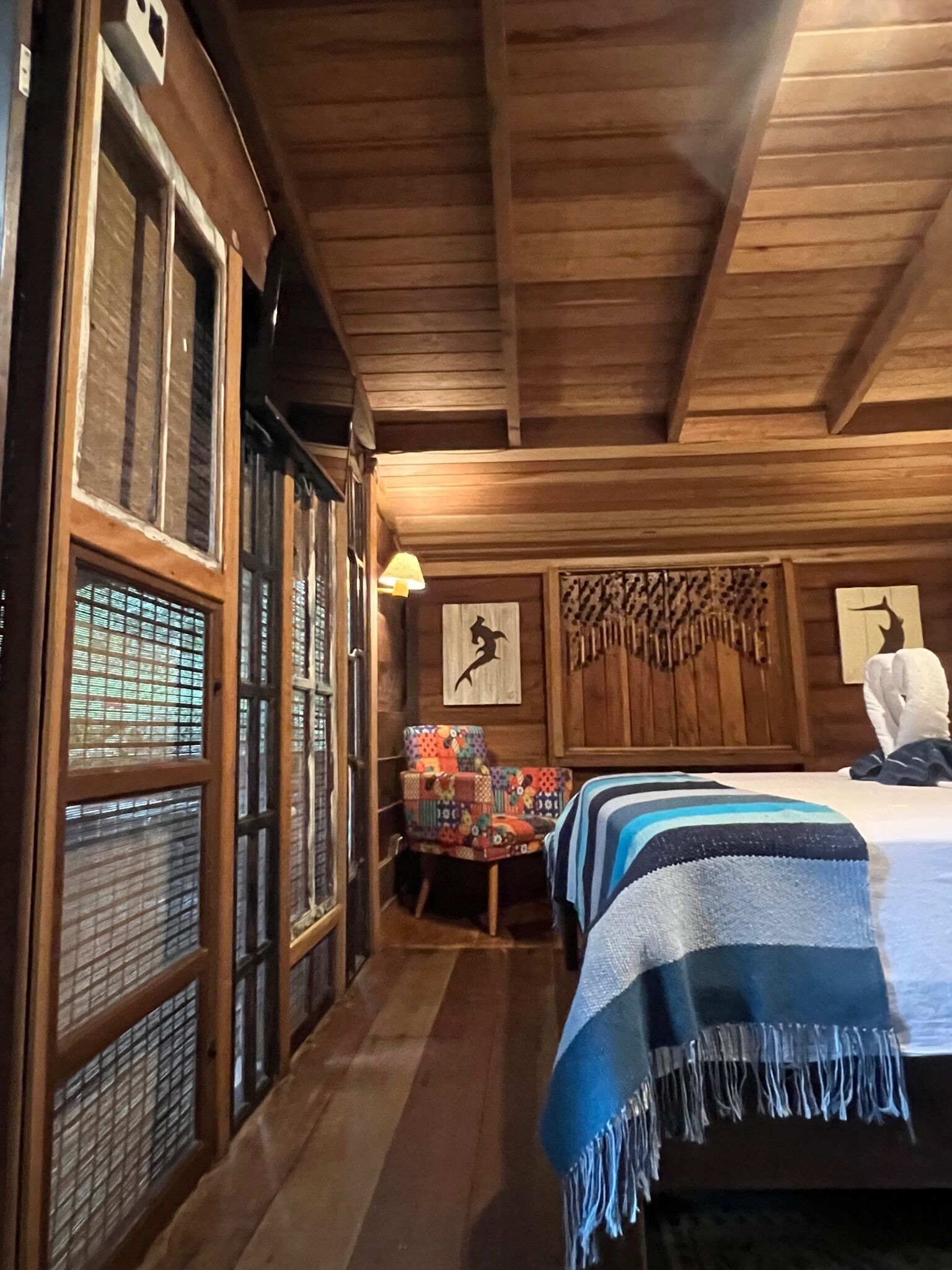 A wooden cabin room with a bed, a chair, and a wall with wooden panels.