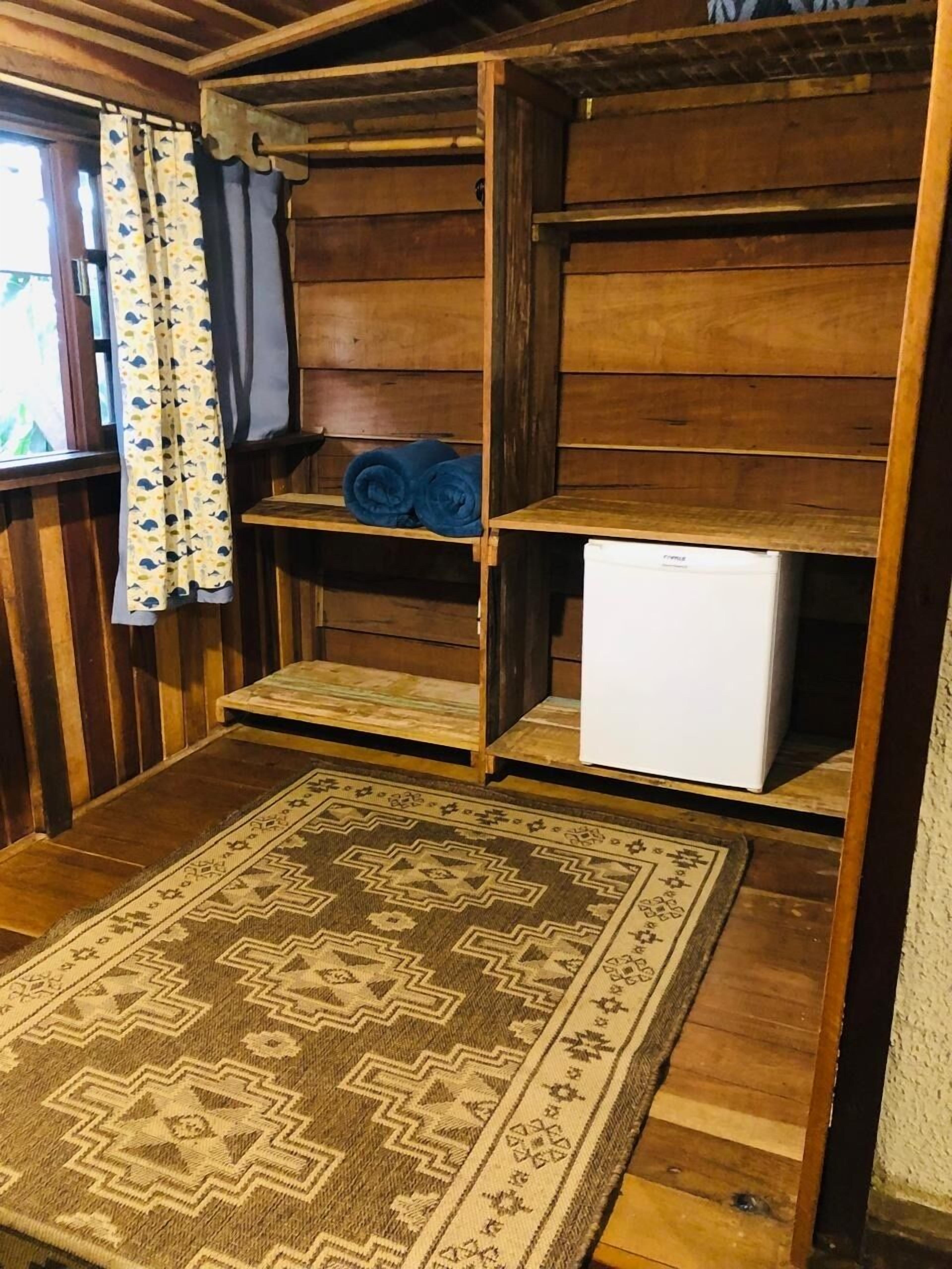 Ein Holzblockhaus-Interieur mit einem gemusterten Teppich, einem weißen Kühlschrank und einem Regal mit zusammengerollten Handtüchern.