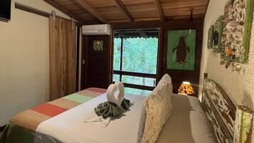 Una habitació acollidora amb sostre de fusta, un llit amb edredó blanc, una decoració mural verda i una finestra amb vista a vegetació.