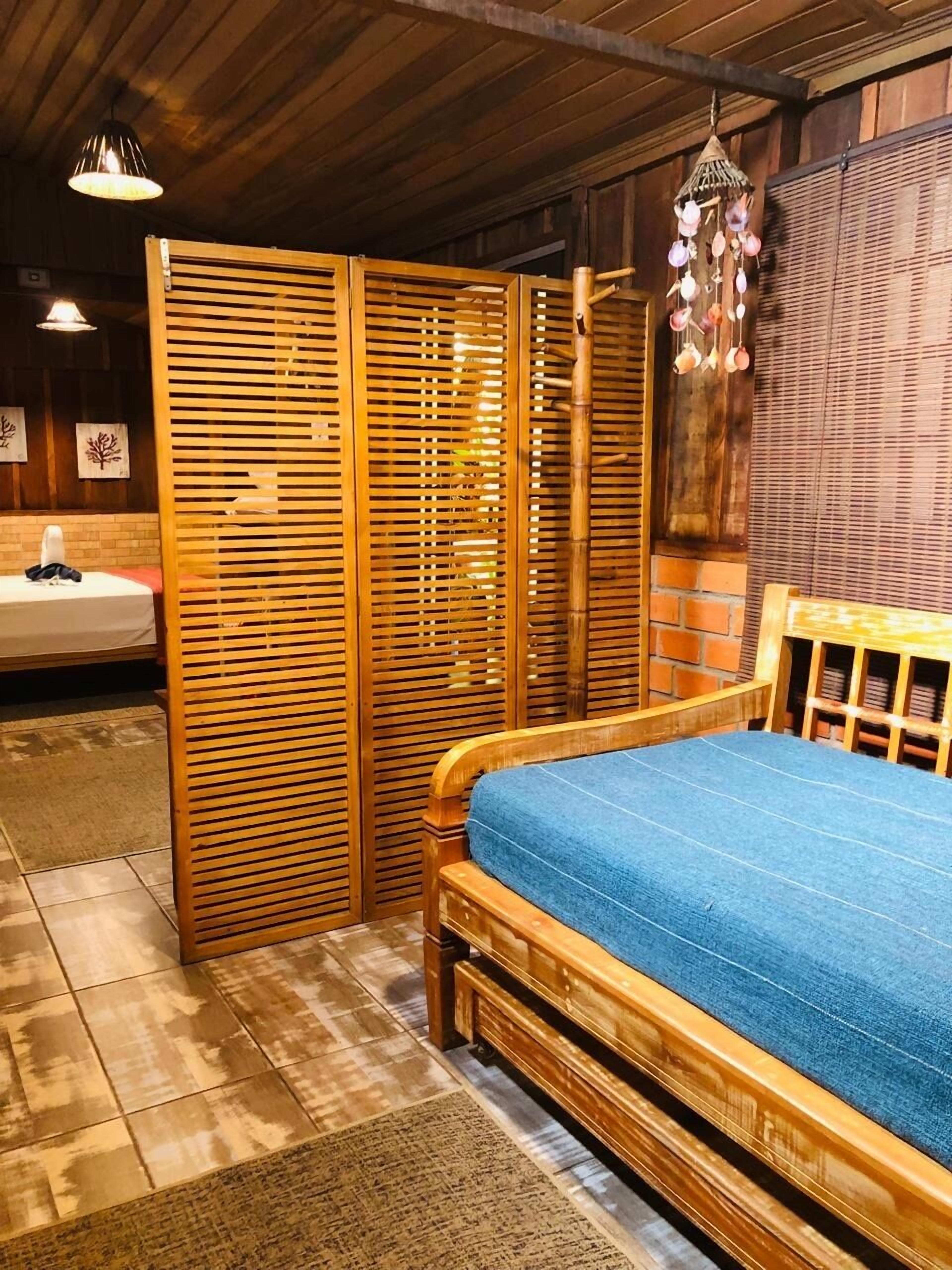 Un lit en bois avec un matelas bleu, une armoire en bois et un luminaire suspendu.