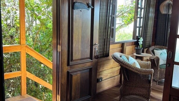 A wooden interior with a large window, wicker furniture, and a door with a welcome sign. - Pousada Praia do Farol (Paranaguá)