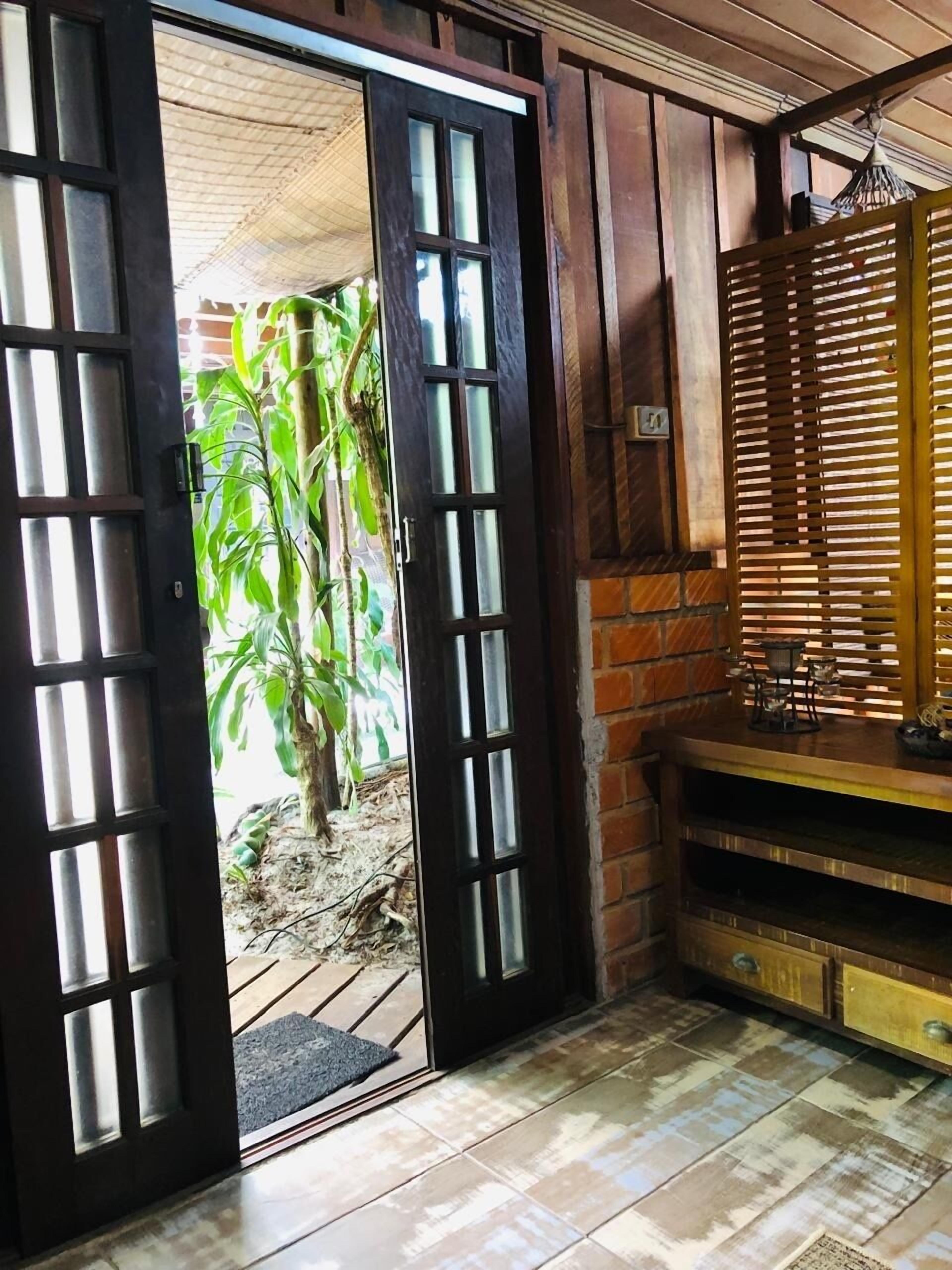 A room with a wooden door leading to a garden, a brick wall, and a tiled floor.
