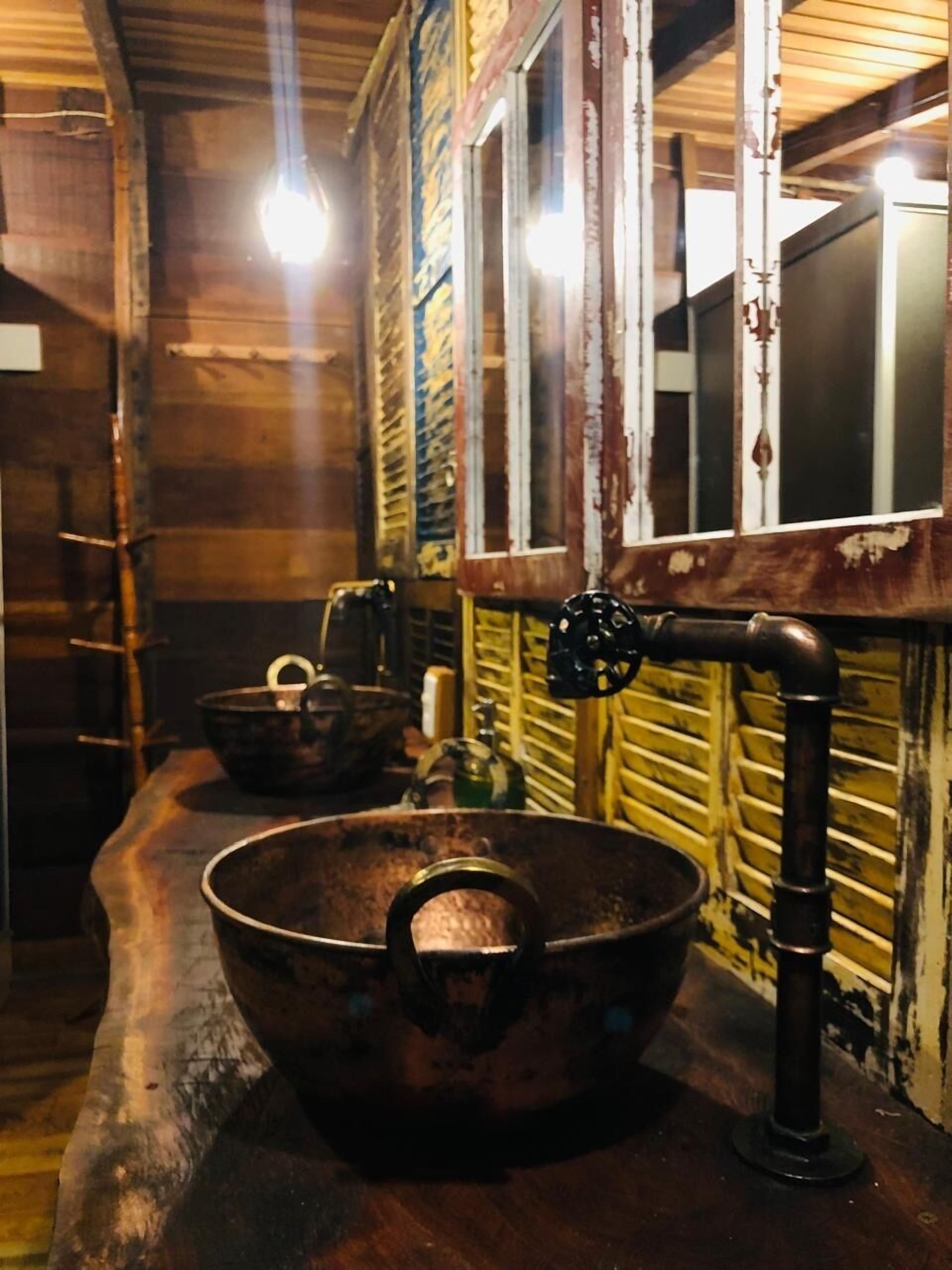 A rustic kitchen with a large copper pot, wooden walls, and a window with a metal frame.