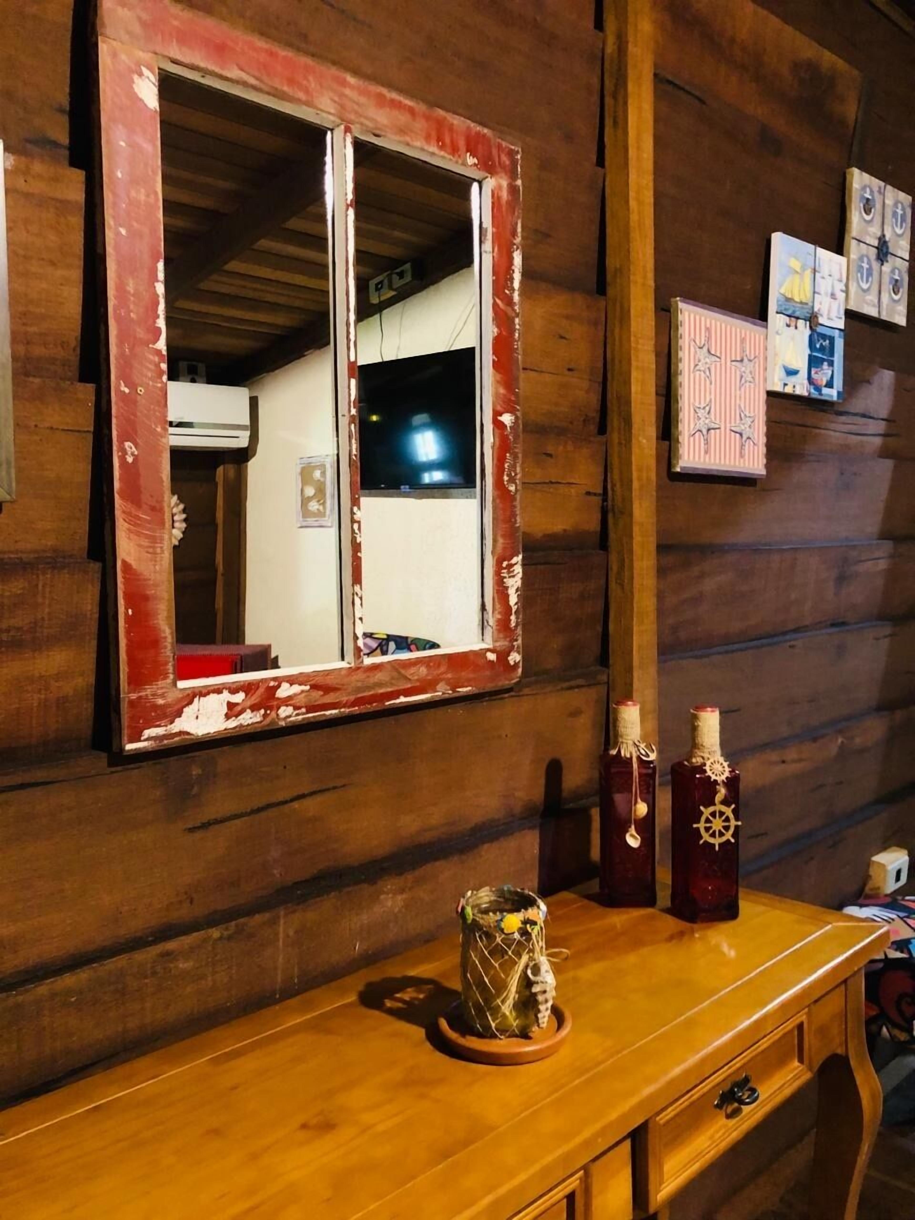 A wooden cabin interior with a rustic mirror, a wooden dresser, and decorative bottles.