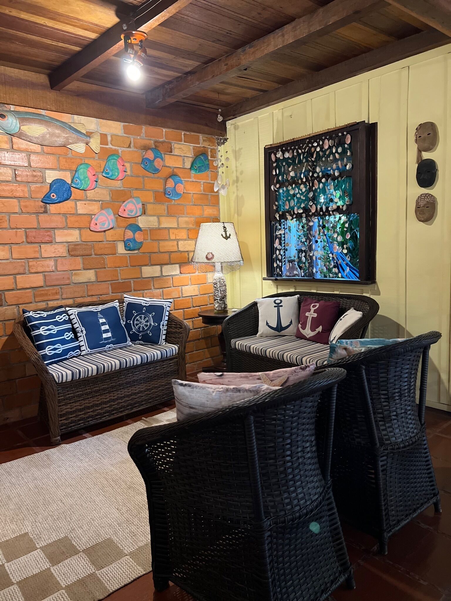 Una habitación acogedora con muebles de mimbre, una pared de ladrillo con adornos de peces y un ventanal con vistas al mar.