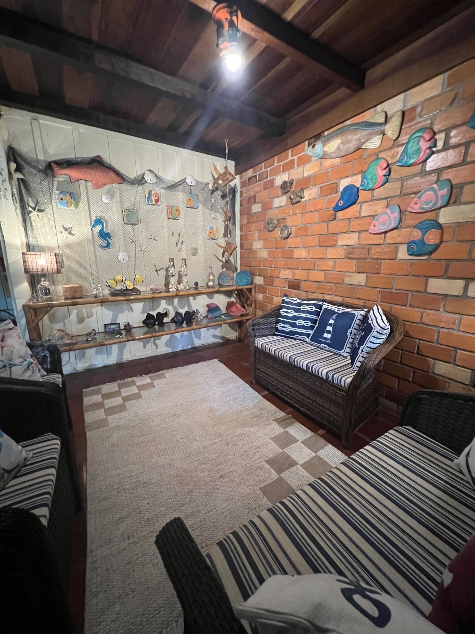 Um quarto acolhedor com parede de tijolos decorada com arte de peixes, um sofá de vime e uma estante de madeira com diversos objetos.