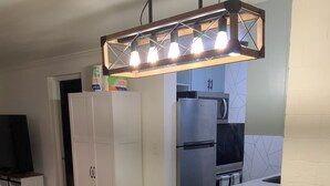 Una cocina moderna con una isla central, taburetes de bar, horno empotrado y una lámpara colgante.