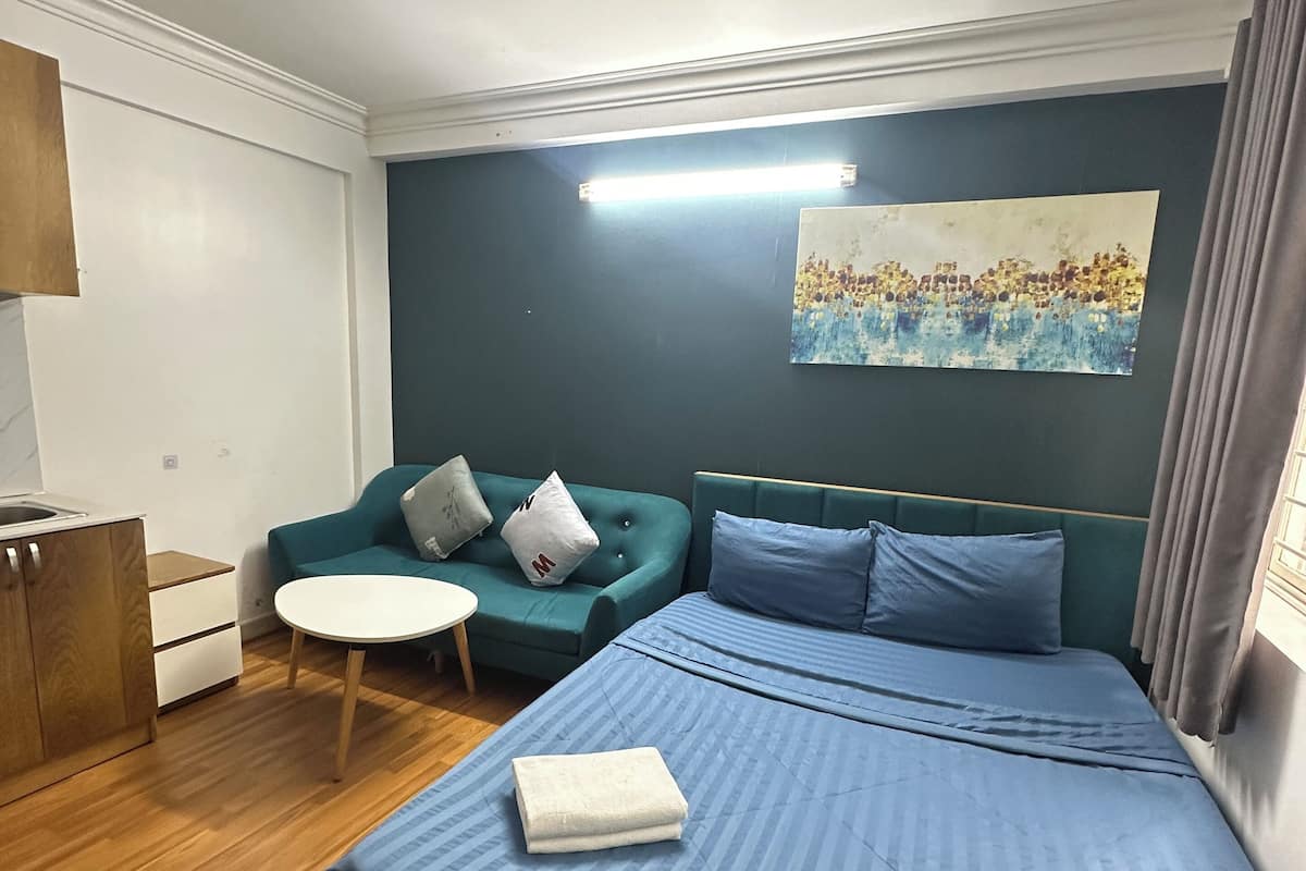 A bedroom with a bed, a green sofa, a small round table, and a painting on the wall.