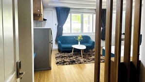 Ett kompakt bostadsutrymme med ett litet kök, en blå soffa, ett litet runt bord och ett trägolv.