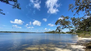A calm lake with clear water, surrounded by trees and a sandy beach.