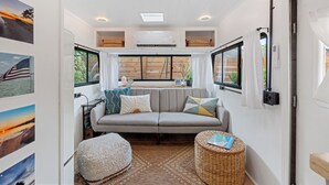 A cozy interior with a sofa, ottoman, and wicker side table, a ceiling fan, and a window with curtains.