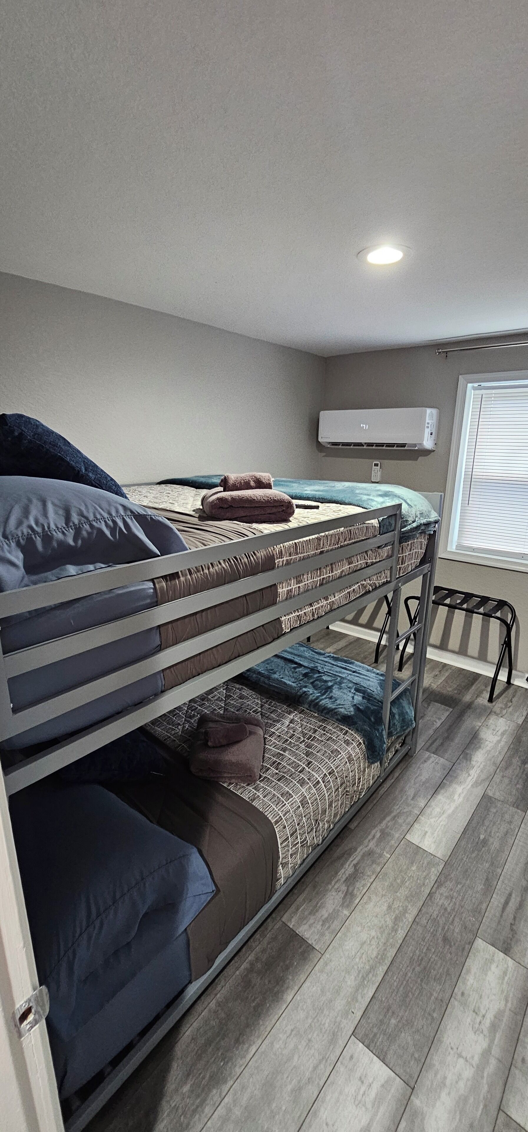A bunk bed room with a ceiling light, air conditioning unit, and a window with blinds.