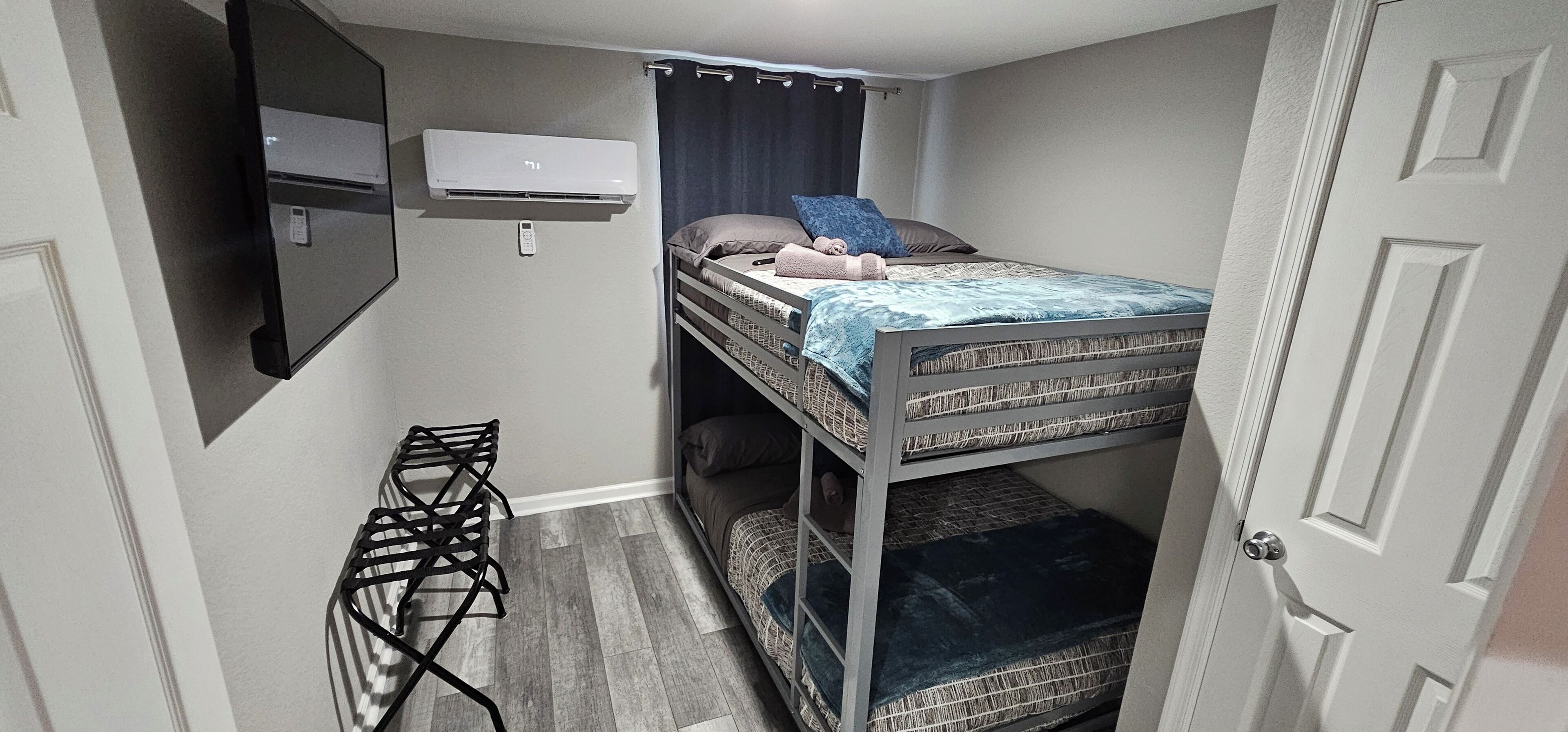 Habitación compacta con literas, aire acondicionado de pared, una mesita y una puerta.