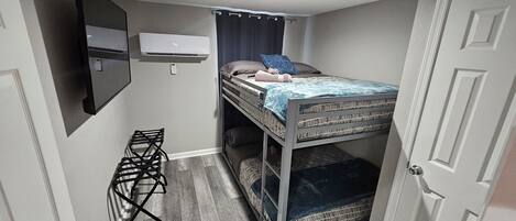 Habitación compacta con literas, aire acondicionado de pared, una mesita y una puerta.