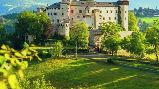 A castle with multiple towers, surrounded by lush greenery and mountains in the background. - Vidora Apartments - Dolomites Escape (Fie allo Sciliar)