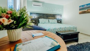 Una camera da letto moderna con un letto, un comodino, un piccolo mobile TV nero, una pianta in vaso e una finestra.