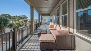 A covered balcony with wicker furniture, large windows, and a view of palm trees and houses.