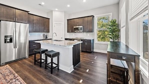 A modern kitchen with dark wood cabinets, stainless steel appliances, and a central island with stools.