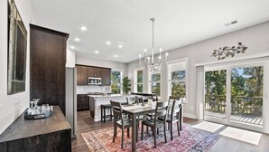 A modern kitchen with a central island, dining area with chairs, and large windows offering a view of the outdoors.