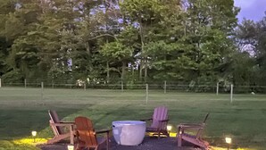 Un espace extérieur verdoyant avec un foyer, deux fauteuils Adirondack et une table en pierre.