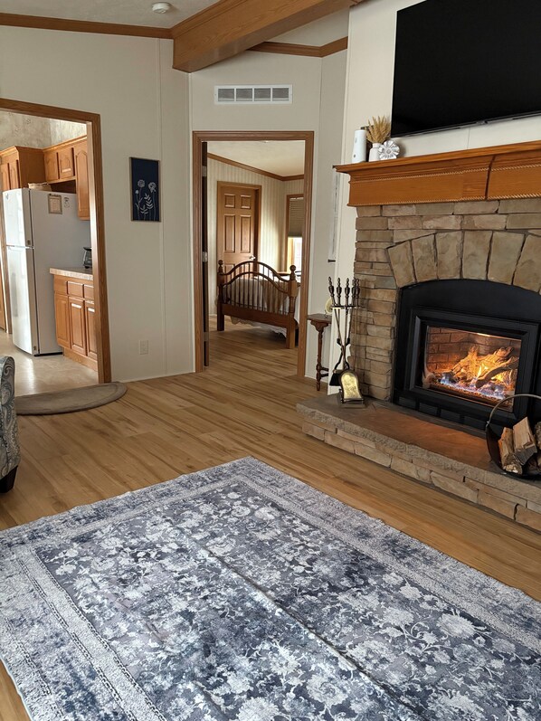 A spacious living room with a fireplace, wooden flooring, and a large rug.