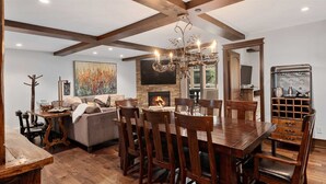 A dining area with a wooden table and chairs, a fireplace, and a modern chandelier. - 5 Bedroom in the Heart of Vail Village (Vail)