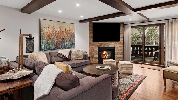 A cozy living room with a fireplace, a large painting, and a balcony with outdoor furniture. - 5 Bedroom in the Heart of Vail Village (Vail)