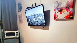 Un televisor montado en la pared, un microondas sobre un soporte, y un cuadro de flores.
