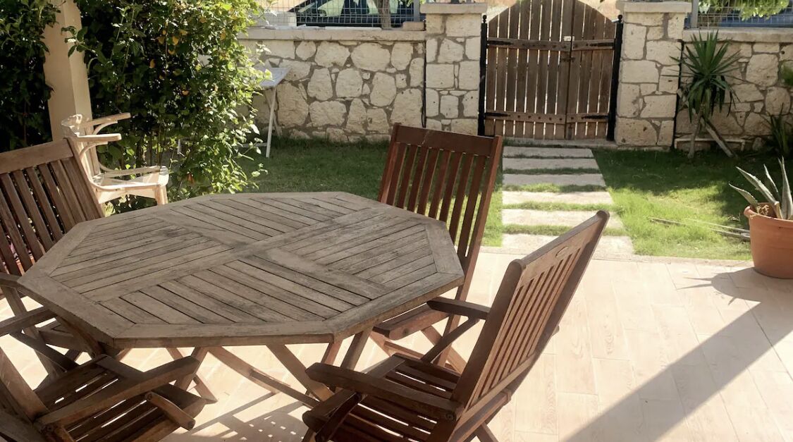Une terrasse extérieure avec une table et des chaises en bois, des murs en pierre et un portail en arrière-plan.