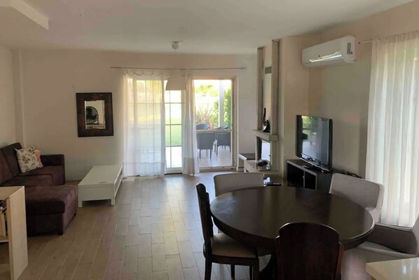 A living room with a dining table, sofa, TV, and an air conditioning unit.