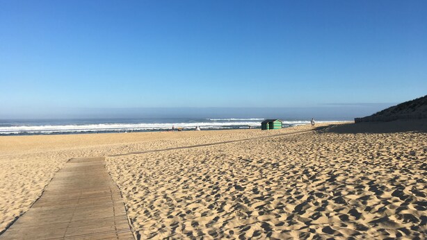 Un'ampia spiaggia sabbiosa con una passerella in legno e una piccola costruzione verde.
