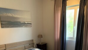 Una camera da letto con un letto, un comodino, una lampada, una finestra con tende e un quadro appeso al muro.