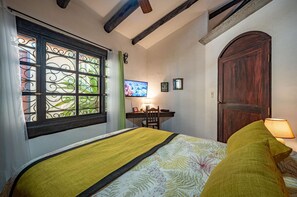 A bedroom with a bed, a desk, a television, and a wooden door.