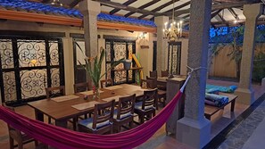An outdoor dining area with a wooden table and chairs, a hammock, and a poolside seating area.