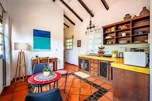 Cozinha com piso ladrilhado, armários de madeira, área de refeições com mesa e cadeiras, e um quadro na parede.