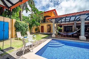 Piscina com borda azulejada, uma rede e área de varanda com cadeiras e mesa.