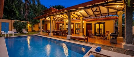 A poolside area with a covered seating area, lounge chairs, and a dining setup.