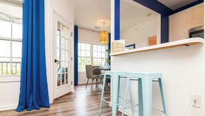 Une pièce avec un plancher en bois, un rideau bleu, une porte blanche, une table à manger avec des chaises et un tabouret bleu.