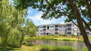 Un immeuble d’appartements à plusieurs étages, doté de balcons, d’un étang et d’une végétation luxuriante.