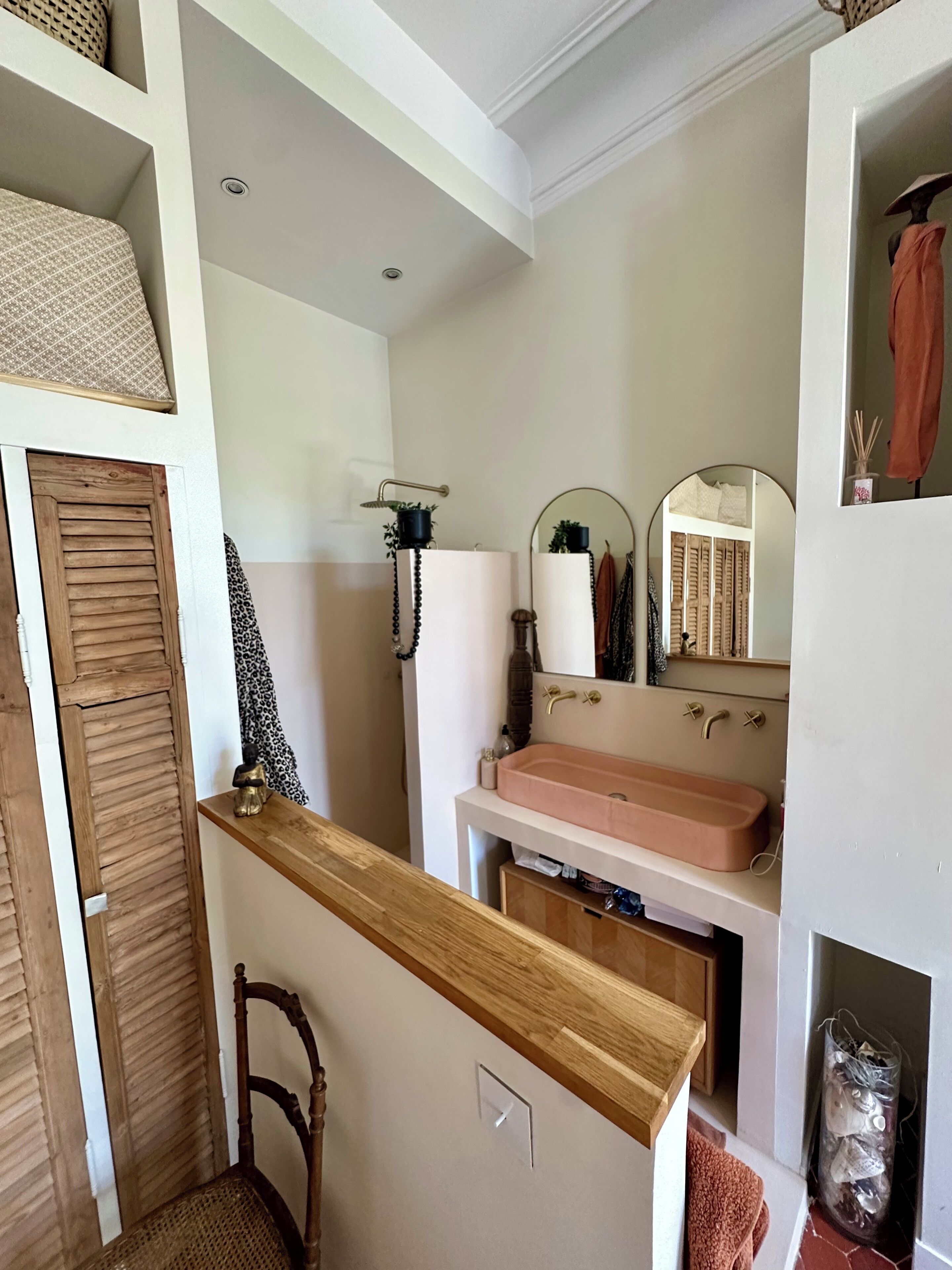 Un baño con tocador de madera, lavamanos rosa, espejo y perchero.