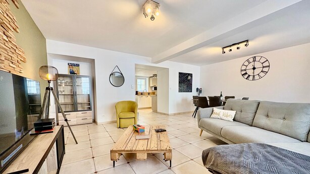 A modern living room with a sofa, coffee table, and a TV. There is a kitchen area in the background.