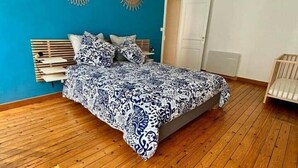 A bedroom with a bed, wooden floor, two wall sconces, and a door.