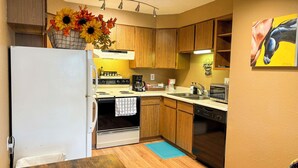 A compact kitchen with wooden cabinets, a white refrigerator, a stove, and a dishwasher.
