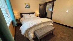 A hotel room with a bed, a bench, a nightstand, a lamp, a painting, and a door with a mirror.