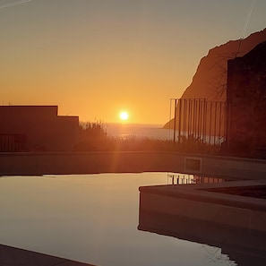 Un coucher de soleil sur une étendue d’eau calme, avec une côte lointaine et un bâtiment doté d’un balcon.